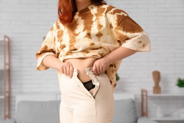 Image of woman trying to do her trousers up after pregnancy weight gain Egham