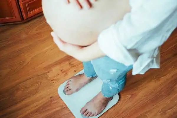 Image of woman weighing herself and experiencing weight gain through pregnancy Egham